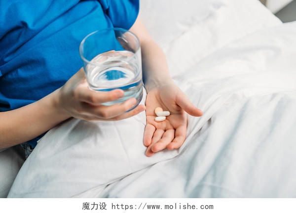 男孩抱着杯水和药品在病床上